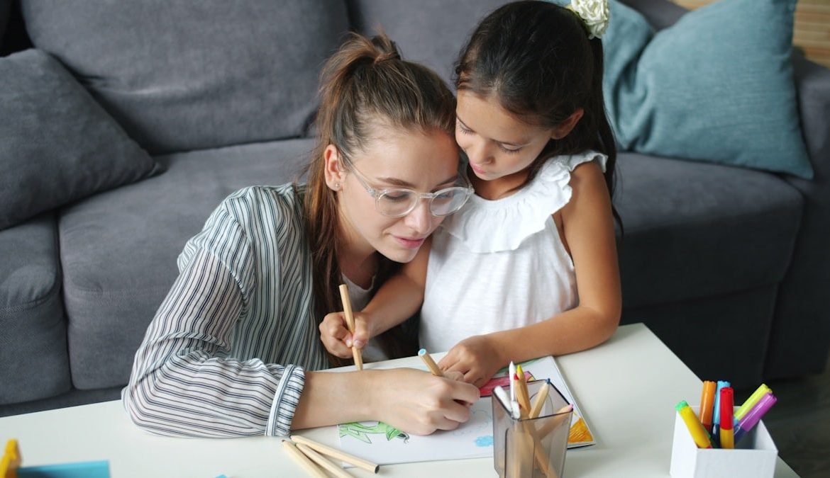 Adorable child and pretty young woman are drawing picture at home enjoying art and leisure time in house together. Family activities, children and happiness concept.